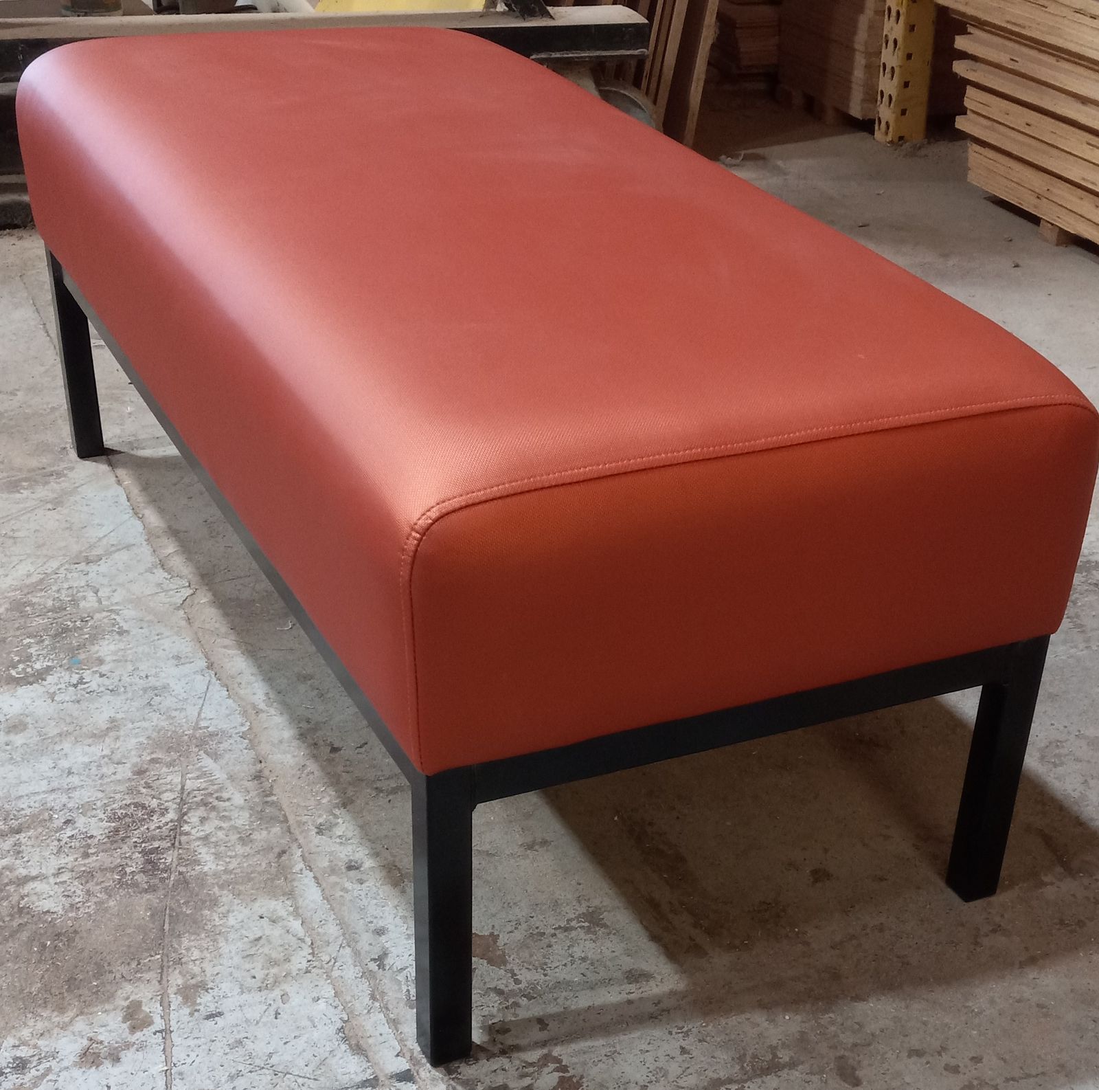 Angle view showing the curved profile of the rust-orange office bench on its black steel frame