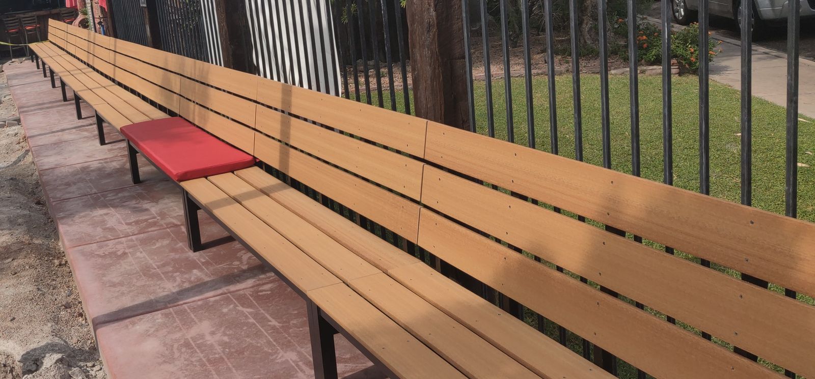 Long wood-slat outdoor bench on a black steel frame, installed on a patio